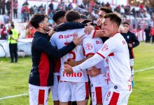 Jogadores de futebol comemoram juntos durante uma partida ao ar livre.