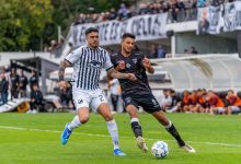 Dois jogadores disputam a bola durante uma partida de futebol em campo aberto.