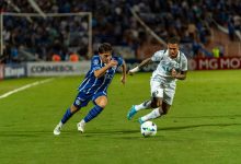 Jogadores disputam a posse de bola durante uma partida de futebol em um estádio iluminado.